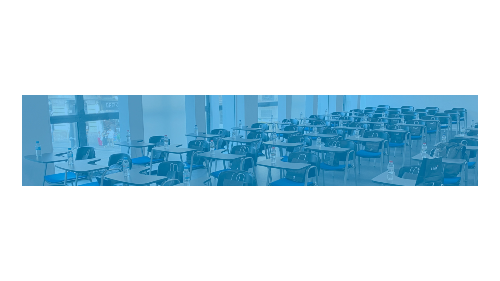 Aula de formación con filas de pupitres azules y botellas de agua bajo un filtro azul traslúcido.