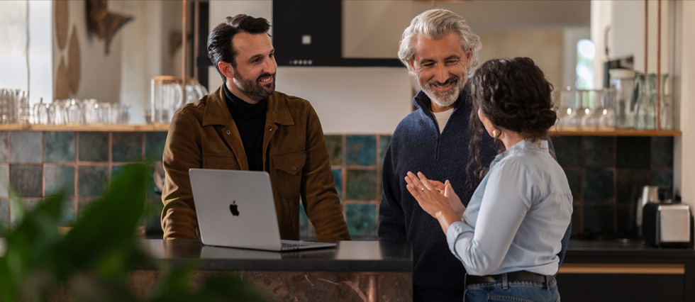 Tres profesionales conversando en un entorno moderno con un MacBook, representando colaboración y consultoría empresarial.